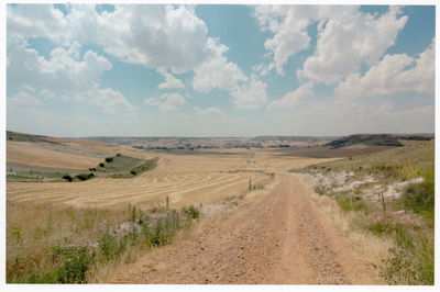 Dirt road passing through landscape against sky