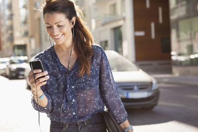 Happy businesswoman using mobile phone while listening music on street