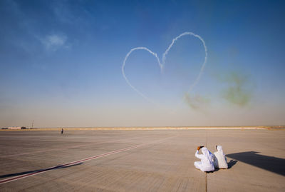 Men photographing heart shape contrail against sky