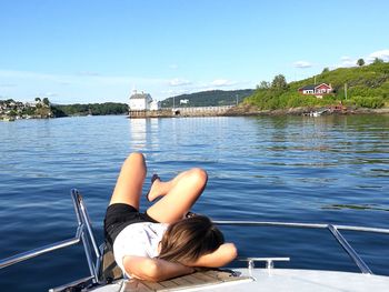 Woman lying on boat sailing in lake against clear sky