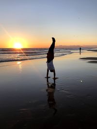 Acrobatics at beach against sky during sunset