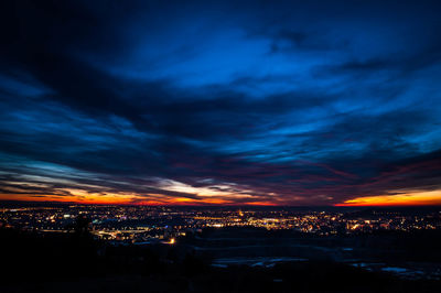 Illuminated cityscape against cloudy sky