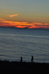 Silhouette people standing on beach against sky during sunset