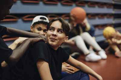 Smiling teenage boy looking at male friend in basketball court