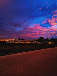 Road by electricity pylon against sky during sunset