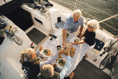 High angle view of male and female friends toasting wineglasses at table in boat
