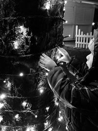 Man standing by illuminated tree against building at night