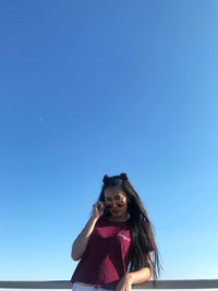 Portrait of smiling young woman against clear blue sky