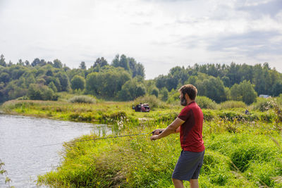 A man with a beard is fishing on the river, casting a line.