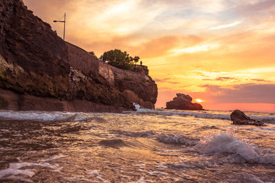 Rocks on beach against sky during sunset
