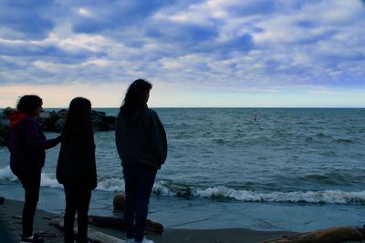 Rear view of people standing on beach against sky