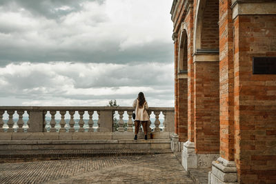 Rear view of women standing on railing against cloudy sky in treia