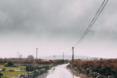 Road by electricity pylon against sky