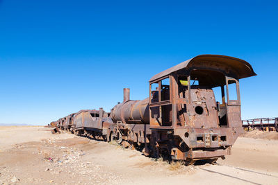 Abandoned train on land against clear blue sky