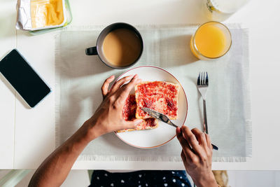 Top view of anonymous african american person spreading jam on fresh toast while sitting at table and having breakfast at home person