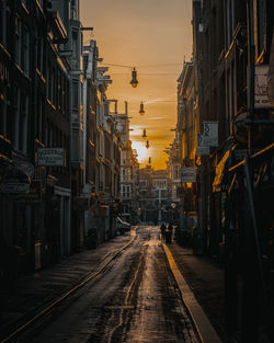 Empty road amidst buildings against sky during sunset