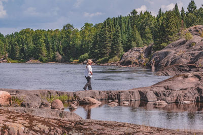 Man standing on rock by trees against sky