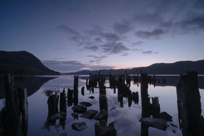 Wooden posts in lake against sky during sunset