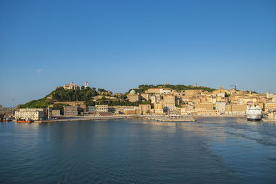 Buildings by sea against clear blue sky