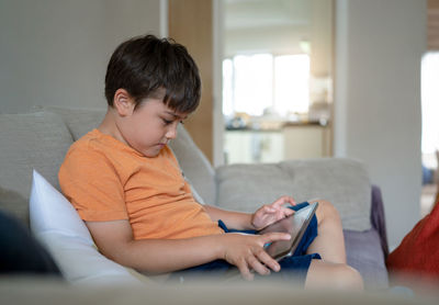 Kid sitting on sofa using tablet learning online on internet, child boy playing game on touch pad,