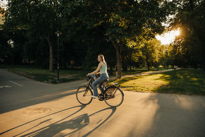 Side view of teenage girl riding bicycle on road at park during sunset