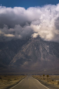 Country road along landscape and mountains against sky