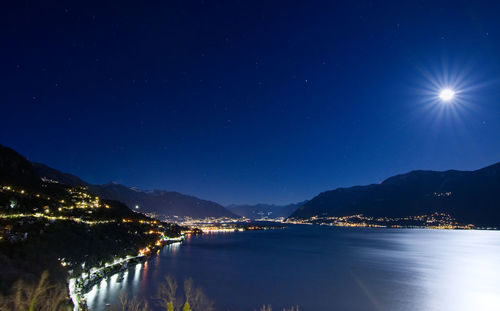 Illuminated lake by mountains against sky at night