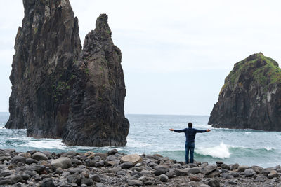 Rear view of man with arms outstretched standing at beach against sky