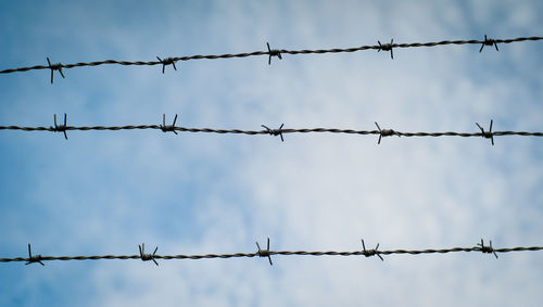 Low angle view of barbed wires against sky
