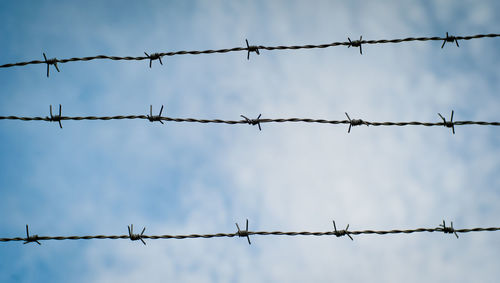 Low angle view of barbed wires against sky