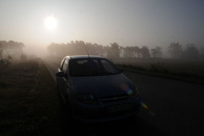 Car on road by field against sky during sunset