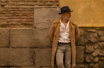 Adult man in coat standing in front of yellow and brick wall on street. madrid, spain