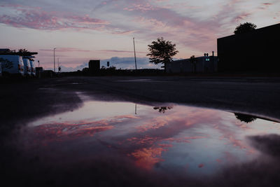 Reflection of silhouette trees in puddle against sky