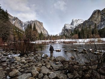 Man standing on rock by lake against sky during winter