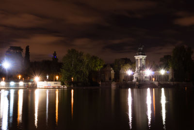 Illuminated buildings by trees against sky at night