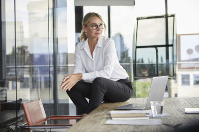 Successful businesswoman sitting on desk, contemplating