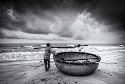 Men pulling traditional boat at beach against cloudy sky