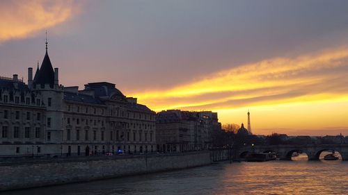Bridge over river in city against sunset sky
