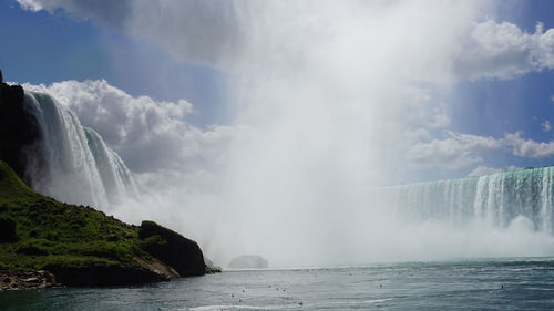 Scenic view of waterfall against cloudy sky