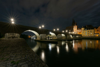 Illuminated buildings by river against sky at night