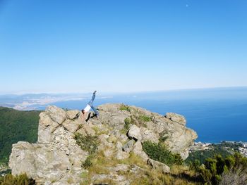 Full length of man exercising on rocks against clear sky