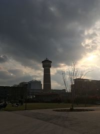 Lighthouse by buildings in city against sky at dusk