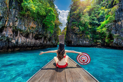 Rear view of woman sitting on rock by lake