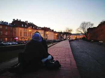 Rear view of woman sitting against sky in city