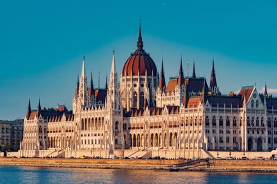 Hungarian parliament building by river against blue sky