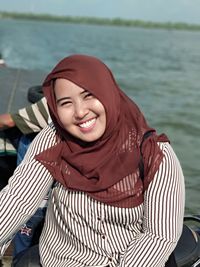 Portrait of smiling young woman sitting by sea