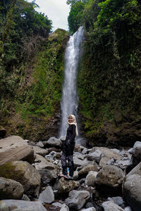 Woman standing on rock against waterfall