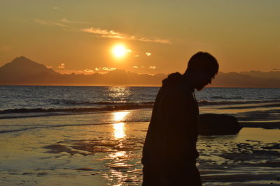 Silhouette man standing on beach against sky during sunset