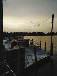 Silhouette pier over river against sky at sunset