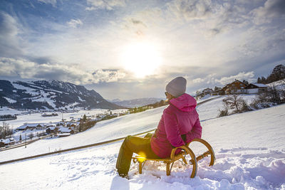 Woman sitting on snowcapped mountain against sky
